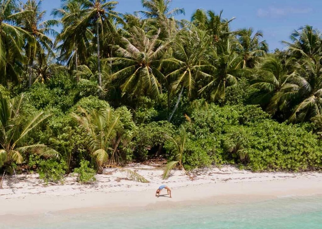 haciendo acrobacias en la playa de una isla local de Maldivas junto al mar turquesa y de fondo la vegetación de una isla local, llena de palmeras de un verde vibrante