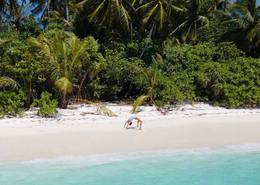 haciendo acrobacias en la playa de una isla local de Maldivas junto al mar turquesa y de fondo la vegetación de una isla local, llena de palmeras de un verde vibrante